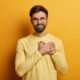 handsome bearded guy keeps hands heart expresses sincere emotions appreciates help heartwarming words stands thankful wears casual yellow jumper poses indoor body language concept 80x80